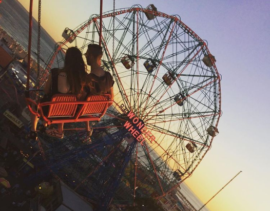 Image of two people in flying chairs ride Coney Island in front of Wonder wheel